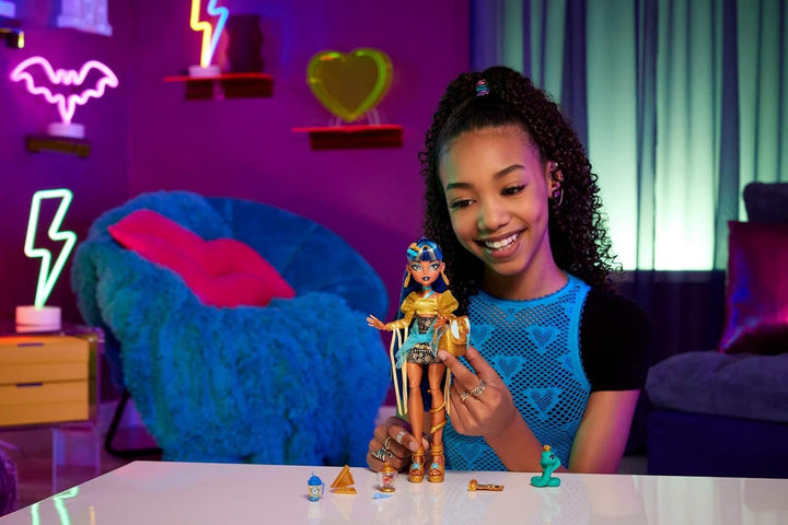 Păpușă Monster High Cleo De Nile în bluză aurie și fustă stratificată, include animal de companie Cobra Hissette și accesorii precum rucsac, gustare și rolă de hârtie, HXH74